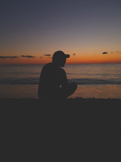 日落时坐在海滩上的男人的剪影